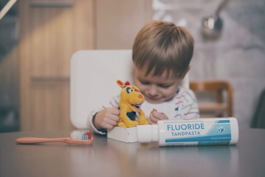 Kinder tandenborstel en fluoride tandpasta naast speelgoedpop op een tafel voor mondverzorging